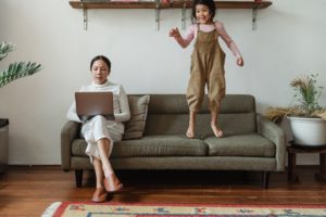 women working from home as child jumps on couch